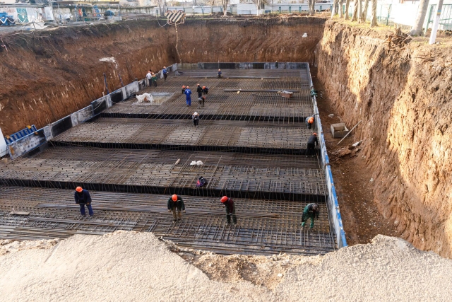 Workers laying reinforced concrete in a deep dig size of a football field